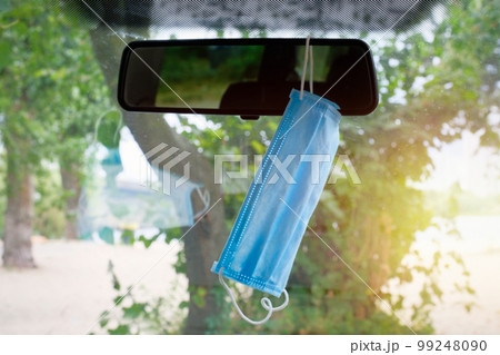 A medical protective mask hangs on the car mirror to protect against bacteria and viruses 99248090