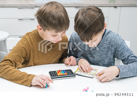 Happy schoolboys play toy constructor sitting at table. Kids read game rules. Collect details on plastic playing board. Happy schoolboys play toy constructor sitting at table. Kids read game rules. Collect details on plastic playing board. 99249311