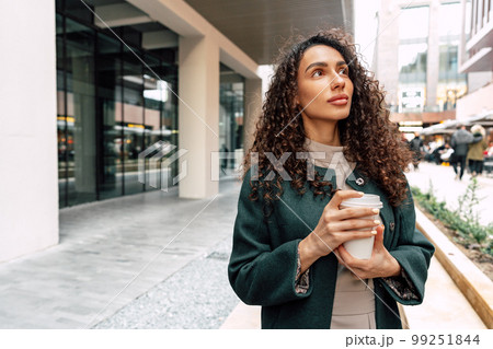 Young and cheerful woman walking with coffee cup through the city 99251844