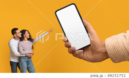 Cheerful Arabic Couple Pointing At Big Blank Smartphone In Giant Female Hand 99252752