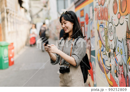 Young Asian woman backpack traveler using mobile phone, enjoying street cultural local art wall. Traveler checking out side streets. Young Asian woman backpack traveler using mobile phone, enjoying street cultural local art wall. Traveler checking out side streets. 99252809