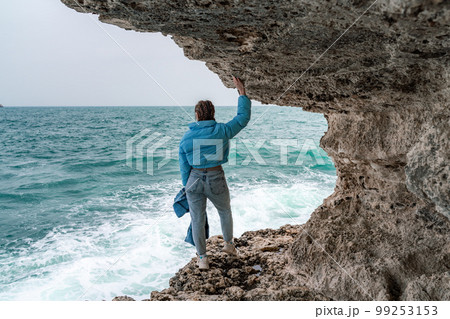 A woman in a blue jacket stands on a rock above...の写真素材 [99253153] - PIXTA