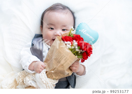 母の日にカーネーションの花束をママに渡そうとしながら恥ずかしがって顔を隠す赤ちゃん 99253177