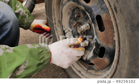 hands of an auto mechanic in gloves put a nut on a stud in the structure of an old wheel with traces of rust close-up, tire replacement in the off-season fragment of the process 99256102