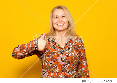 Photo portrait of nice caucasian woman with bright smile showing thumb up in patterned dress isolated on yellow colored background. 99256591