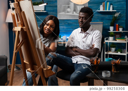 Drawing female teacher supervising artwork of african american male student in arts classroom. Friends learning together art of sketching with colored pencils at home modern atelier. Drawing female teacher supervising artwork of african american male student in arts classroom. Friends learning together art of sketching with colored pencils at home modern atelier. 99258308