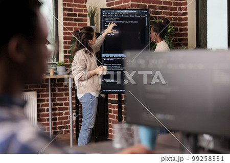 Team of coders talking about algorithms in front of big screen, analyzing html script language. Software developers discussing database on terminal window working in it programming agency 99258331