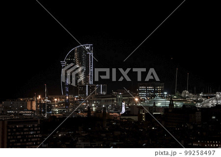 Distant view of illuminated W letter on top of luxurious W Barcelona Hotel and buildings under sky at night in Barcelona, Spain 99258497