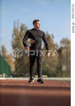 Athletic man walking through the stadium with victory cup Athletic man walking through the stadium with victory cup 99259332