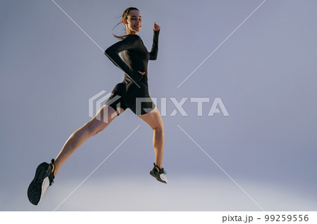 Smiling sporty woman running in Mid-Air exercising during cardio workout over studio background 99259556