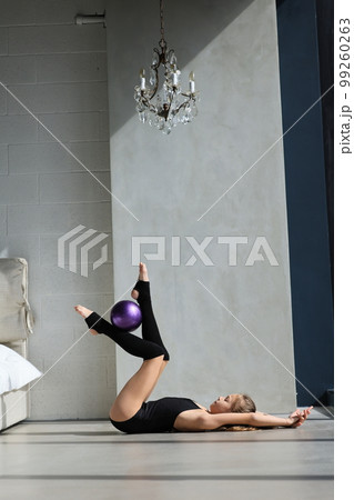girl gymnast in black body and leggings is training with a purple gymnastic ball. children's professional sport. Rhythmic gymnastics girl gymnast in black body and leggings is training with a purple gymnastic ball. children's professional sport. Rhythmic gymnastics 99260263