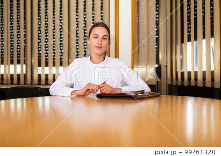 Portrait of a young woman sitting at a table in a conference room with a folder of documents 99261320