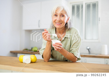 Mature woman eating tasty yogurt in kitchen 99262245