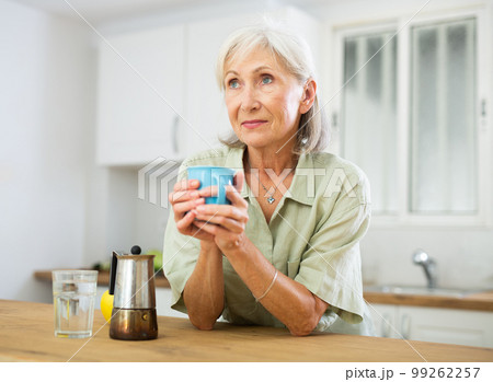 Positive old woman drinking coffee in kitchen at home 99262257