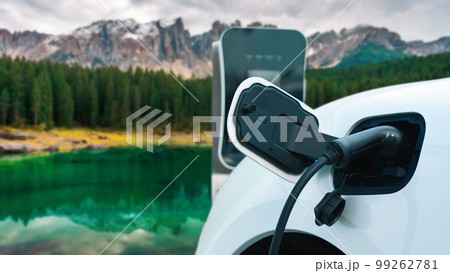 Progressive travel concept by EV car in remote mountain with charging station. 99262781