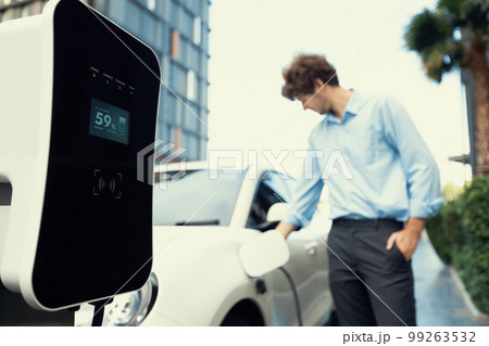 Progressive concept of focus EV car at charging station with blur man background Progressive concept of focus EV car at charging station with blur man background 99263532