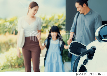 Focus home charging station for EV car, blur progressive family in background. Focus home charging station for EV car, blur progressive family in background. 99263633