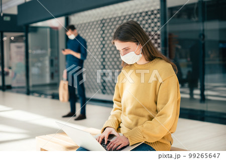 female blogger in a protective mask works on a laptop 99265647