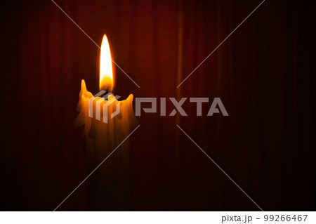 Single yellow wax candle burning alone in the dark red 99266467