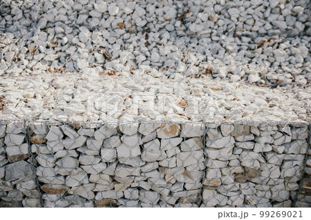 Granite stones behind a metal grate for strengthening the slope. Stones behind the wire. grey texture. construction. 99269021