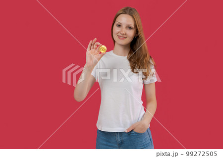 Smiling young business woman in white shirt holding bitcoin in hand posing 99272505