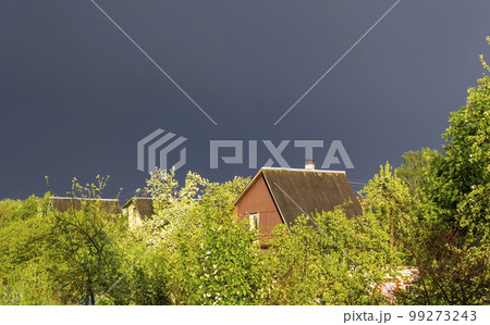 Stormy sky over a small village. The green foliage is illuminated by the sun. 99273243