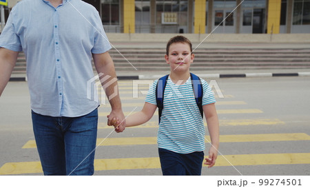 boy son holding his father hand crosses road through pedestrian crossing. happy family concept. dad helps child boy cross road school lesson. zebra road. first grader with school bag back. happy boy 99274501