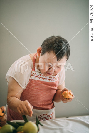 elderly woman with down syndrome is studying in the kitchen peels tangerines elderly woman with down syndrome is studying in the kitchen peels tangerines 99276974