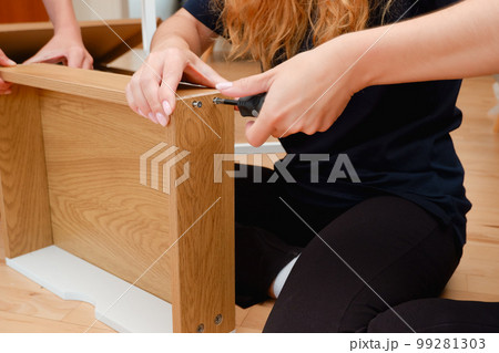 Woman hold screws collects wooden furniture details seated on warm floor in living room, close up. 99281303