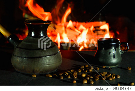 Cezve and coffee cups with coffee beans on the background of a burning fire. Turkish coffee. 99284347