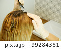 Hair coloring at home. The girl herself dyes the regrown hair roots. 99284381