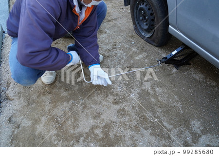 車のパンクでスペアタイヤに交換するのにジャッキアップしている男性 99285680