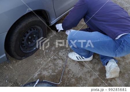 車のパンクでスペアタイヤに交換するのにジャッキアップしている男性 99285681