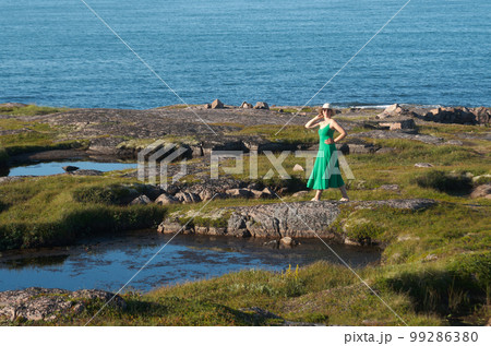 Woman tourist in a straw hat and a green dress on the seashore on a bright sunny day Woman tourist in a straw hat and a green dress on the seashore on a bright sunny day 99286380