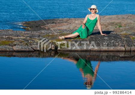 Woman tourist in a straw hat and a green dress on the seashore on a bright sunny day 99286414