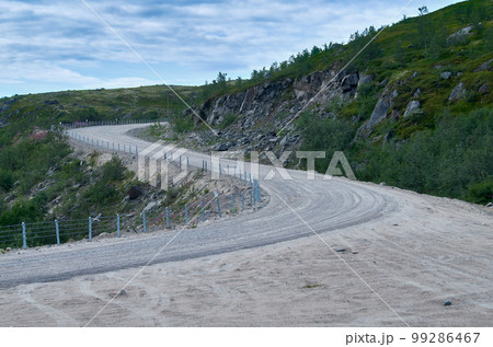 Winding dirt road in a mountainous area under a summer cloudy sky 99286467