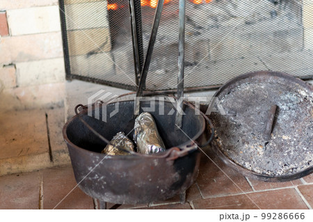 山小屋の暖炉で古いダッチオーブンを使い焼き芋を焼いているところ 99286666