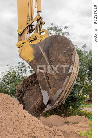 A bucket of excavator pours the ground into a heap against the background of a rural industrial zone. Bulldozer work on the construction site 99288019