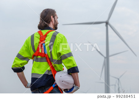 man engineer holding helmet safety wearing uniform standing at wind turbine. man engineer holding helmet safety wearing uniform standing at wind turbine. 99288451