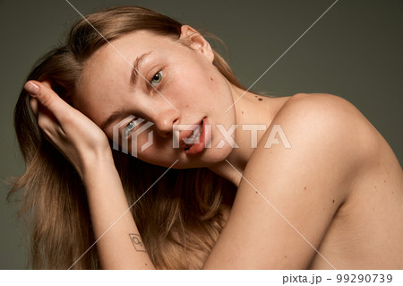 Closeup portrait of beautiful young girl with smooth clear skin and without makeup looking at camera with tenderness over grey background. Concept of natural beauty 99290739