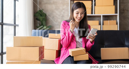 Startup SME small business entrepreneur of freelance Asian woman using a laptop with box Cheerful success happy Asian woman her hand lifts up online marketing packaging and delivery SME idea concept 99290744