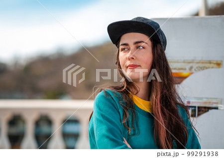 Portrait of a young pretty Caucasian woman in a cap and sportswear, looking into the distance. Street in the background. The concept of advertising and business Portrait of a young pretty Caucasian woman in a cap and sportswear, looking into the distance. Street in the background. The concept of advertising and business 99291938