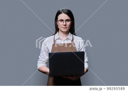 Young woman in apron using laptop on grey studio background 99293589