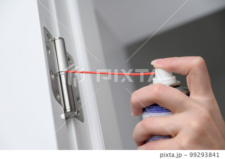 A man greases door hinges. A worker lubricating the closer adjustment. A man greases door hinges. A worker lubricating the closer adjustment. 99293841