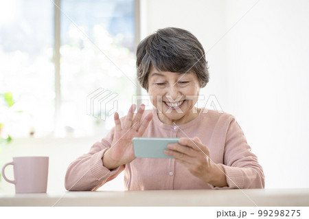 スマートフォンに向かって手を振る高齢の女性 99298275