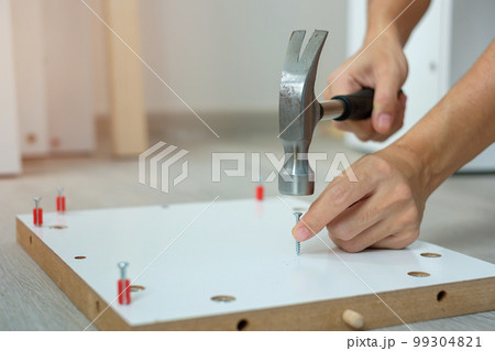 man using hammer hammering a nail into wooden boards, assembling or repairing furniture at home. DIY, Renovation, repairing and development home or apartment concepts 99304821