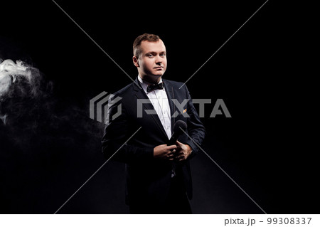 Man in costume holding microphone, posing on dark background, actor, singer, show, host of event 99308337