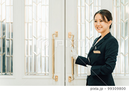 結婚式場のドアを開けるウェディングプランナー・ドアスタッフ・ホテリエの女性(結婚式スタッフ) 結婚式場のドアを開けるウェディングプランナー・ドアスタッフ・ホテリエの女性(結婚式スタッフ) 99309800