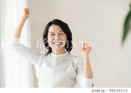 窓辺でガッツポーズをするミドル女性 99310172