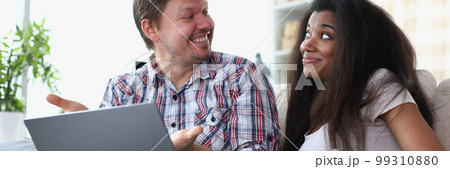 Interethnic family couple laughing and chatting while sitting on sofa at home with laptop. Interethnic family couple laughing and chatting while sitting on sofa at home with laptop. 99310880